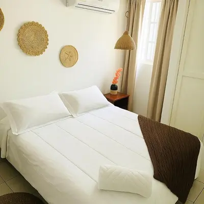 a white bed in a bedroom with a clock on the wall at Habitación en apartamento compartido al frente del cc Unico in Barranquilla