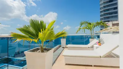 a balcony with white furniture and palm trees on a building at Penthouse Marea Con Jacuzzi Privada Vista Mar in Cartagena de Indias