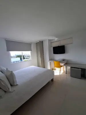 a white bedroom with a bed and a desk and a television at Hotel Mar del Plata in Cartagena de Indias