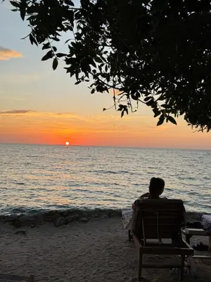 a person sitting on a bench on the beach watching the sunset at Thani Ecobeach Barú in Playa Blanca