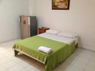 a bedroom with a bed with a green blanket and a refrigerator at Cecil Aparta Estudios in Barranquilla