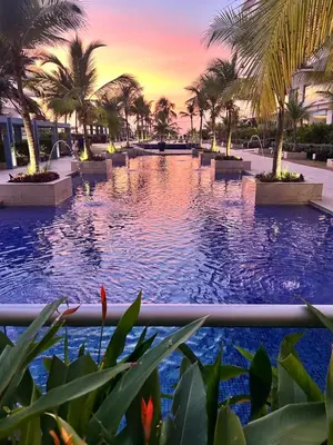 a pool with palm trees and a sunset in the background at Apartamento de lujo Morros ULTRA con vista y acceso directo al mar , Cartagena de Indias in Cartagena de Indias