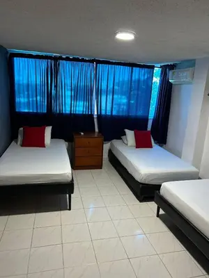 a room with two beds and a window with blue curtains at Hotel Boston Superior in Barranquilla