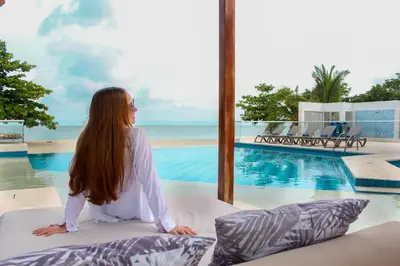 a woman sitting on a bed next to a swimming pool at Exclusiva casa en Baru con piscina y playa privada in Playa Blanca