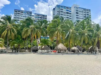 a beach with palm trees and huts and buildings at Perla Santa - Luxury Condo in Santa Marta