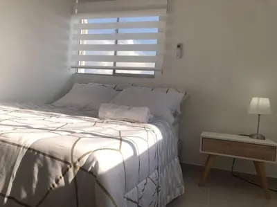 a bedroom with a white bed with a nightstand and a window at Acogedor apartamento en Cartagena/asequible in Cartagena de Indias