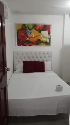 a bedroom with a white bed with a painting on the wall at HOSTAL BARRANQUILLA INN in Barranquilla