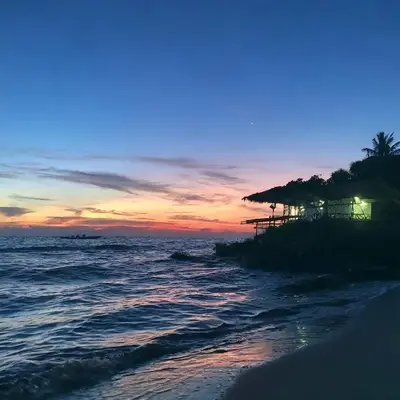 a sunset on the beach with a house and the ocean at Punta Arena EcoHostal & EcoFit - Your Eco-Conscious Oasis in Cartagena de Indias