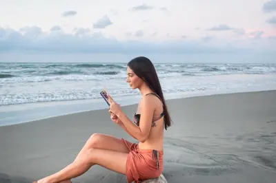a woman sitting on the beach looking at her cell phone at Hotel Playa Palmeras Cartagena - Vía al Mar in Cartagena de Indias