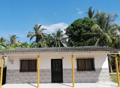 a small white house with palm trees in the background at Cabaña Moñitos cerca al mar e Isla Fuerte in Moñitos