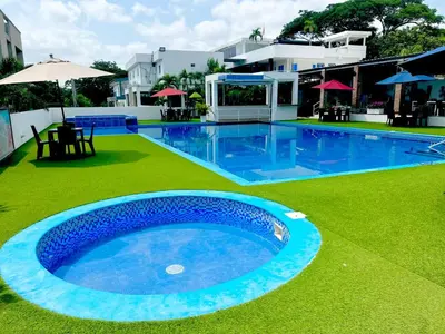 a large blue swimming pool with green grass and umbrellas at Hotel Boutique Chateau de la Mar in Juan de Acosta