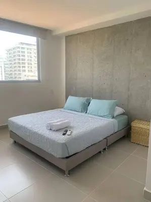a bedroom with a bed with blue pillows and a window at Encanto Rentals at Sunno Beach in Cartagena de Indias