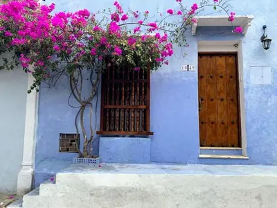 a blue building with a wooden door and pink flowers at Cartagena más cómoda y económica in Cartagena de Indias