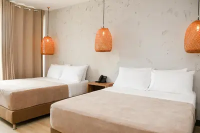 two beds in a hotel room with two lamps at Ciela Hotel in Coveñas