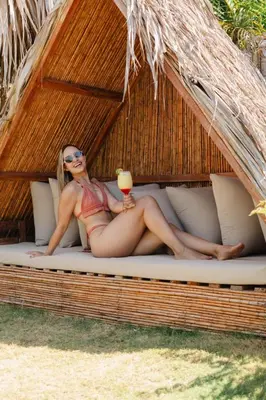 a woman in a bikini laying on a bed with a drink at JERUSALEMA BEACH GLAMPING in Tolú