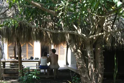 a man and woman sitting on a bench under a tree at Hostel Nugeku in Rincón