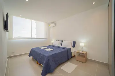 a bedroom with a bed with a blue blanket and a window at 1H Encanto Rentals @ Sunno Beach in Cartagena de Indias