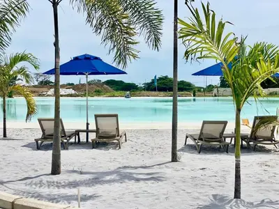 a beach with chairs and tables and blue umbrellas at U-GO Baia Kristal: Oasis Moderno en Cartagena in Cartagena de Indias