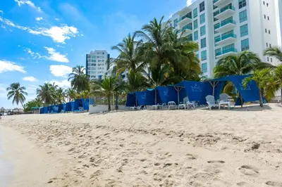 a beach with blue chairs and palm trees and a building at Villa con piscina privada en coveñas sucre in Coveñas
