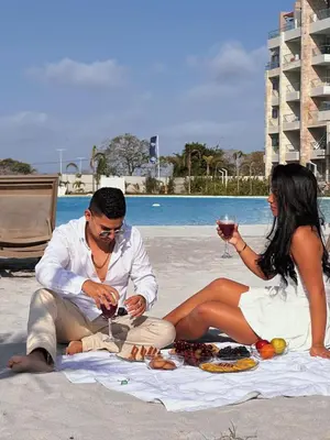 a man and woman sitting on the beach with food and wine at Apartamento 4g Baia Kristal Cartagena in Cartagena de Indias