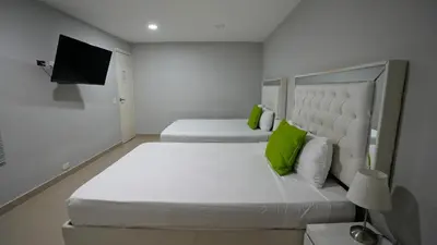 a white bedroom with two beds and a flat screen tv at Hotel Casa Bellamare in Cartagena de Indias