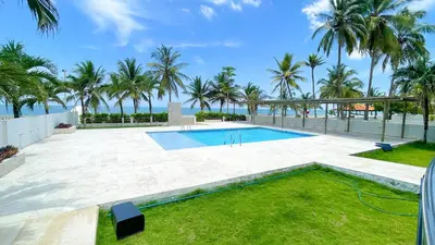 a swimming pool with palm trees and the ocean at Hermoso Apartamento Frente al Mar 3 Habitaciones TR12 in Coveñitas
