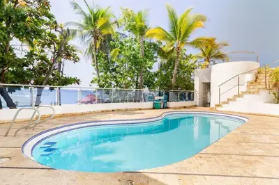 a blue swimming pool with palm trees and the ocean at Playa Mar in Cartagena de Indias