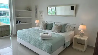 a white bedroom with a bed and a mirror at Apartamento con salida y vista a la playa in Cartagena de Indias