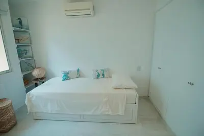 a white bedroom with a white bed with blue pillows at Caribbean Beachfront Getaway in Cartagena de Indias