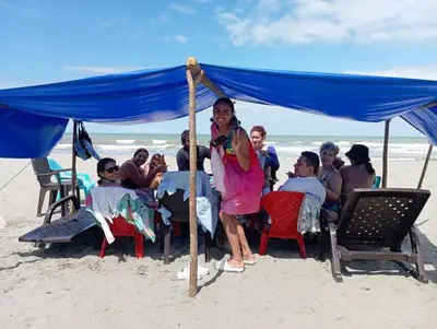 a group of people sitting under a blue tent on the beach at Cabaña Olas Del Mar in San Bernardo del Viento