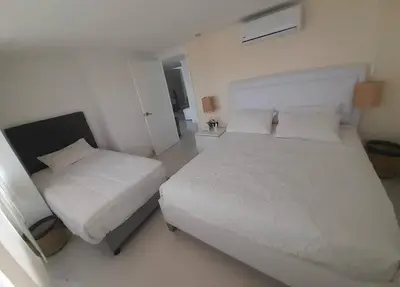 a white bedroom with two beds and a window at Gloria Al Laguito Duplex in Cartagena de Indias