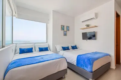 two beds in a white room with a large window at Vista de lujo al mar y la bahía in Cartagena de Indias