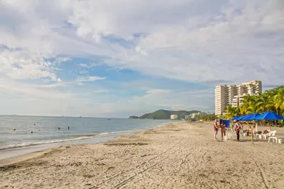 a beach with blue umbrellas and people on the sand at Descanso y playa, cómodo apartamento en Kuali, Santa Marta in Santa Marta
