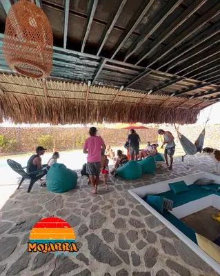 a group of people sitting under a straw umbrella on the beach at KITE en Mojarra Beach Habitación privada vista al mar in Salina de Rey