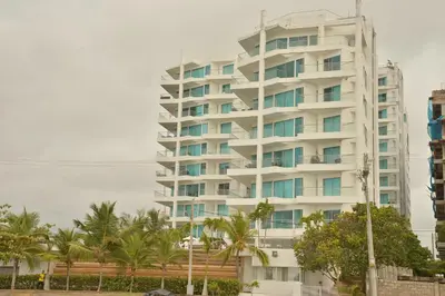 a tall white building with palm trees in front of it at Moderno 3 Alcobas Frente a Playa in Cartagena de Indias