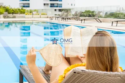 a woman reading a book next to a swimming pool at CB1622 | Suite frente al mar con balcón y piscina in Cartagena de Indias