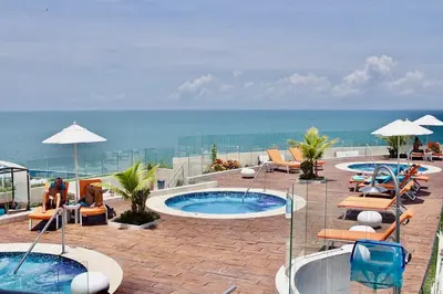 a patio with two pools and lounge chairs and the ocean at Beautiful 2 BR Ocean View Condo in Cartagena in Cartagena de Indias