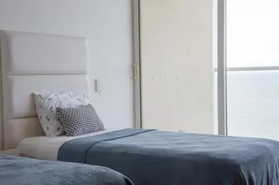 a bedroom with a bed with blue sheets and a window at Luxury apt sea front AC Wifi pool at cartagena in Cartagena de Indias