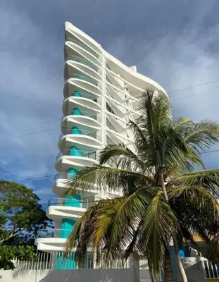 a tall white building with a palm tree in front of it at Espectacular apto frente al mar in Coveñas