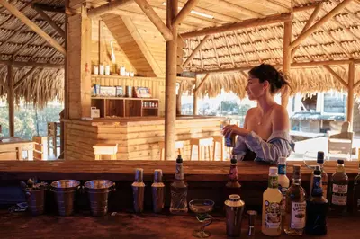 a woman sitting on a bar with bottles of wine at Hotel isla bonita in Tintipan Island