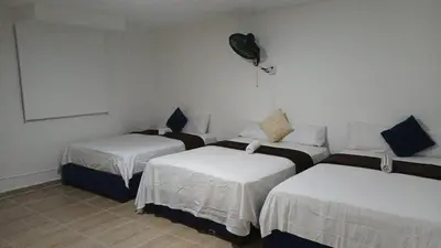 a room with three beds and a fan on the wall at Prado alto inn in Barranquilla