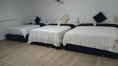 a room with three beds with white sheets and blue pillows at Prado alto inn in Barranquilla