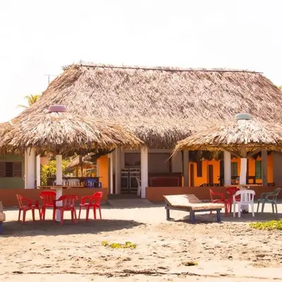 a building with chairs and tables and a straw hut at Cabañas Capilla Del Mar in San Bernardo del Viento