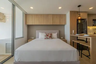 a bedroom with a large white bed and a kitchen at Suite 15th floor con vista mar y piscina CB1511 in Cartagena de Indias