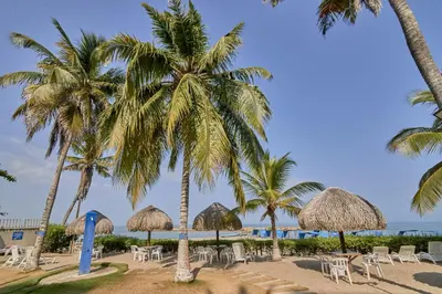 a beach with tables and chairs and palm trees at Hermoso Apartamento Frente al Mar 2 Habitaciones PAZ146 in Coveñitas