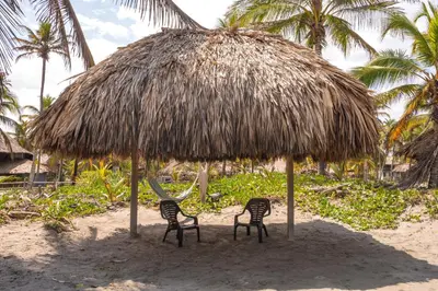 two chairs under a straw umbrella on the beach at Cabaña San Miguel in Moñitos