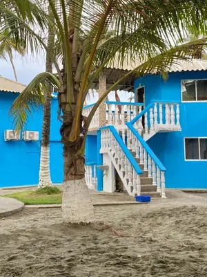 a blue building with stairs next to a palm tree at Cabañas Kosta Azul in San Bernardo del Viento