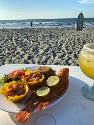 a plate of food on the beach with a drink at Cabañas Kosta Azul in San Bernardo del Viento