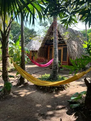 a hammock in front of a thatched hut at Hospedaje VILLA CRETA in Isla Fuerte