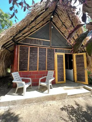 two chairs and a house with a straw roof at Hospedaje VILLA CRETA in Isla Fuerte